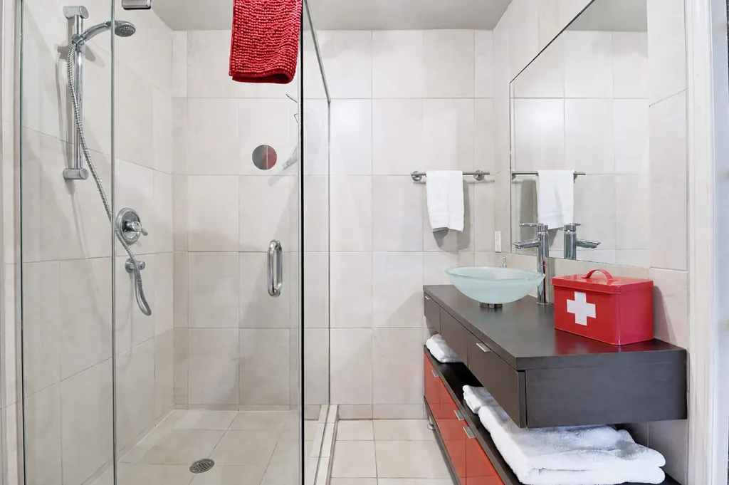 Salle de bain avec grande douche vitrée, vasque en verre et trousse de premiers soins