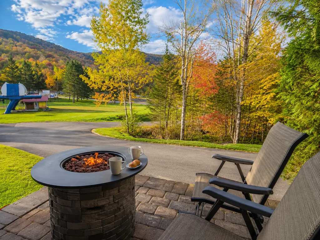 Foyer extérieur allumé sur la terrasse, arbres aux couleurs d’automne et montagne