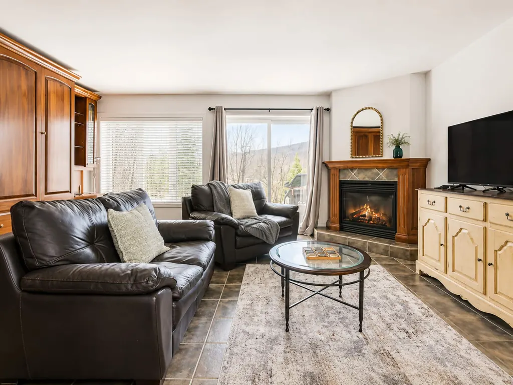 Salon avec foyer au gaz allumé, canapés en cuir et grandes fenêtres sur la montagne